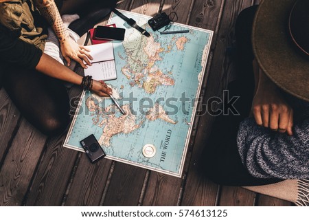 Man and woman discussing tour plans using the world map. Woman making notes and pointing on the map while the man is discussing.