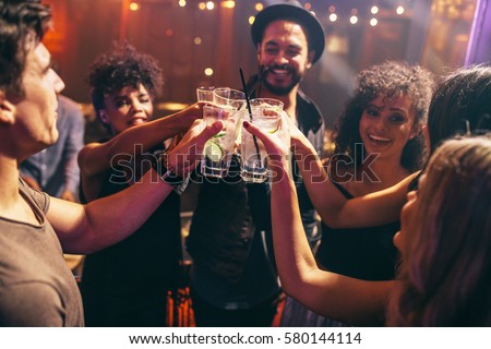 Group of friends having drinks at the night club party. Young people enjoying at a bar toasting cocktails.