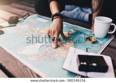 Tourist planning vacation with the help of world map with other travel accessories around. Young woman pointing at North America on the world map.