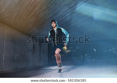 Full length shot of young athlete running under bridge in city. Fit young man jogging in the city.