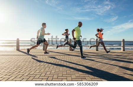Full length shot of young people running along seaside. Group of runners working out on a road by the sea.