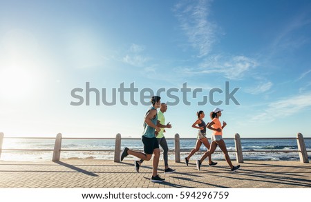Portrait of young runners on the sea front path along the shoreline. Group running along a seaside promenade.