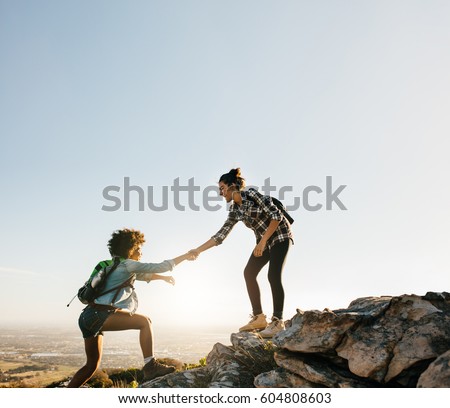 Female friends hiking help each other in mountains. Young female hiker helping friend while trekking in mountain.
