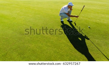 Professional golfer check line for putting golf ball on green grass. Golf player crouching and study the green before putting shot