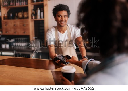 Female customer making payment through mobile phone at counter in cafe with young man. Barista holding credit card reading machine in front of female costumer with cell phone.