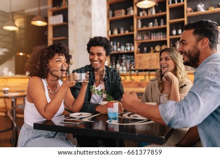 Young friends having a great time in restaurant. Multiracial group of young people sitting in a coffee shop and smiling.