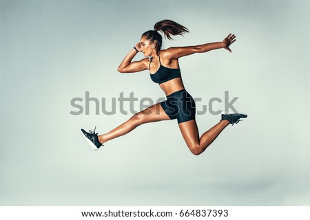 Side view of fit young woman jumping against grey background. Female model in sports wear jumping in air.