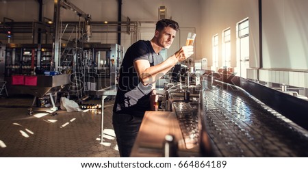 Brewery factory owner examining the quality of craft beer. Young man inspector working on alcohol manufacturing factory checking the beer.