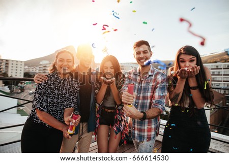 Group of friends hanging out together and blowing confetti on rooftop party.