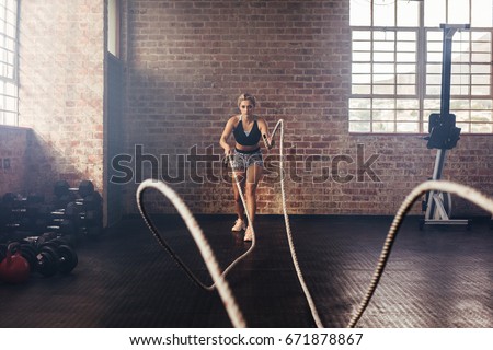 Young woman doing strength training using heavy ropes at the gym. Athlete moving the ropes in wave motion as part of strength training.