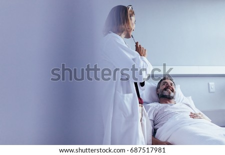 Female doctor talking to male patient lying in hospital bed. Medical professional interacting with patient in hospital ward.