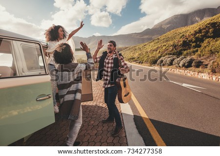 Group of man and women on road trip standing by the van and giving high five. Cheerful friends enjoying themselves on a vacation.