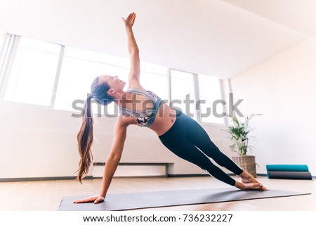 Slim woman in side plank pose at yoga class, Vasisthasana exercise. Female balancing on mat indoors at fitness gym