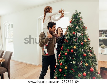 Family decorating a Christmas tree. Young man with his daughter on his shoulders helping her decorate the Christmas tree.