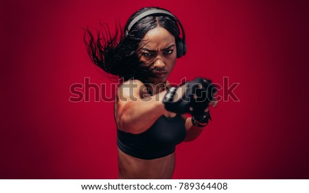 Boxer practicing her punches in a studio. African female boxer practicing boxing against red background.