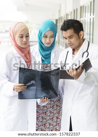 Image of Experienced male doctor guide two female junior doctors examining a file in in front of hospital