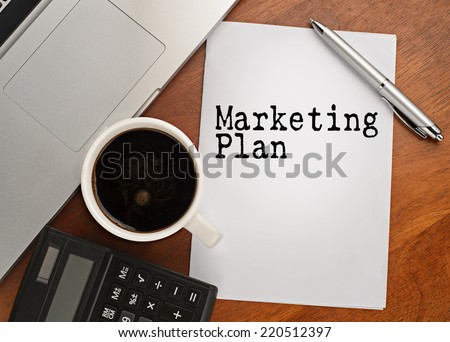 Notebook with text marketing plan on table with coffee, calculator and notebook