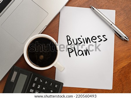 Notebook with text Business Plan on table with coffee, calculator and notebook