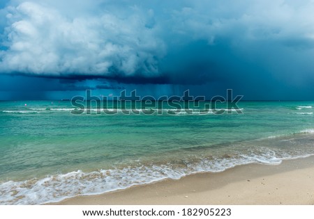 Over the ocean storm with heavy clouds, dramatic sky. White sand of Miami beach.