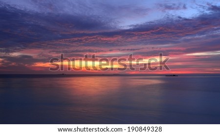 Setting sun painted the sky, clouds, ocean and beach in red, yellow, lilac bright colors
