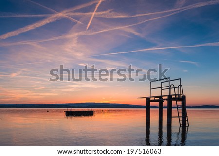 Tower to jump into the water against the backdrop of the setting sun. Reflection of sunlight in the lake. Gorgeous evening sunset colors in the sky and the lake. Lake Zug in central Switzerland.