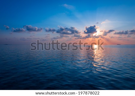 Sunset over the Ocean. Rays of the sun through the clouds. Setting sun painted the sky and ocean in deeply bright   color.
