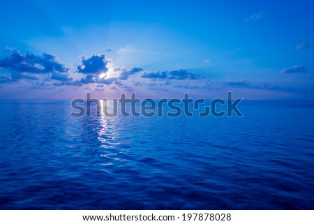 Sunset over the Ocean. Rays of the sun through the clouds. Setting sun painted the sky and ocean in deeply bright   color.