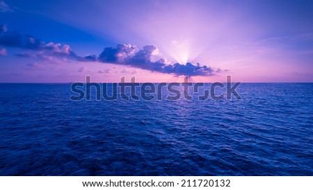 Scenic sunset over the Ocean. Rays of the sun through the clouds. Setting sun painted the sky and ocean in deeply bright  color.