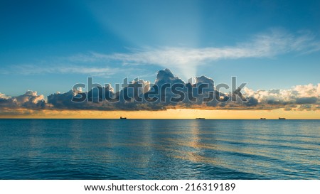 A ocean water surface under cloudy sky. Great impression of distance and solitude. Rays of the rising sun.