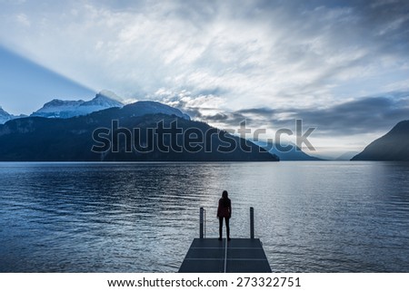 Epic landscape complete with a small woman figure. Mountain, lake and sky in bright colors of sunset