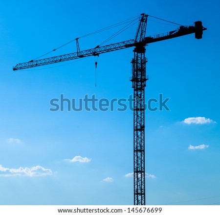 Construction crane silhouette on a blue sky with clouds.