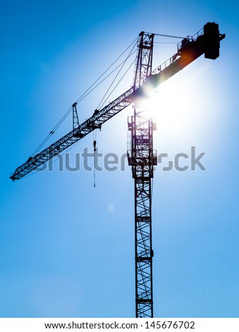 Construction crane silhouette in front of a blue sky with sun light flare.