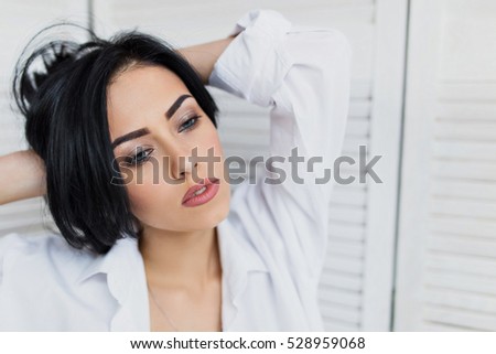 Portrait of sensual brunette woman in white shirt. Worth holding hair in hands
