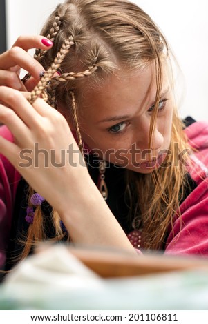 pretty young girl doing a hair with dred pigtail in front of a mirror at home on white background