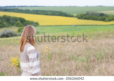 beautiful girl in a field of green grass looking into the distance shielded his eyes from the sun