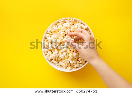Popcorn viewed from above on yellow background. Woman eating popcorn. Human hand. Top view