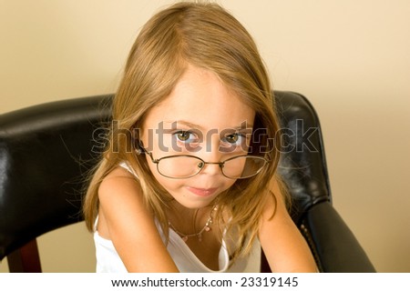 A young girl about 6 pretends to be working while wearing glasses too big for her head.