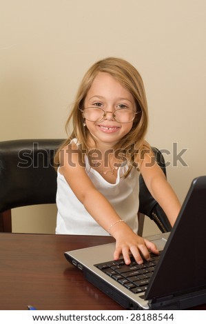 A young girl about 6 pretends to be busy at her notebook computer while wearing glasses too big for her head.