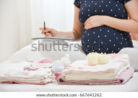 Pregnant woman is packing baby clothes for going to maternity hospital. Woman taking notes