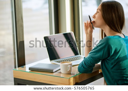 Young woman work at cafe on computer in front of the window