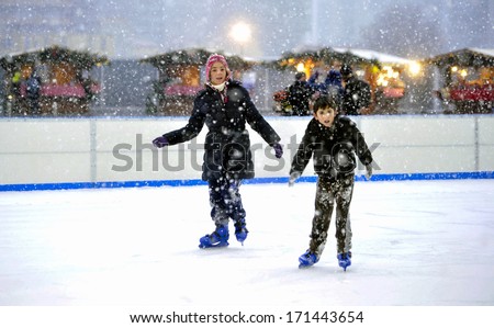 MILAN, ITALY - FEBRUARY 07: a boy and a  girl ice skating in an outdoor public ice skating ring under a snowfall in Milan. February 07, 2009.