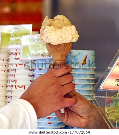 MILAN, ITALY-OCTOBER 11, 2006: Hands serving an italian ice cream waffle cone with ice cream cups in the background.