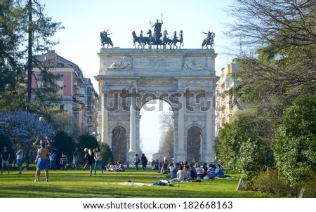MILAN, ITALY-MARCH 17, 2014: Young people laying on the grass, at Sempione Park, for the beginning of springtime,  with the historical monument, Arco della Pace, in the background, downtown Milan.