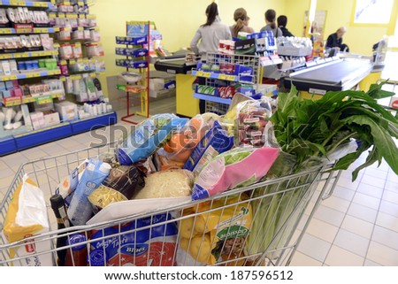 VARESE, ITALY-APRIL 11, 2014: Full shopping cart, and customers paying at the cash register of a supermarket, in Varese.