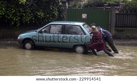MILAN, ITALY-NOVEMBER 26, 2002: people pushing a damaged car out of a flooded road during a flood caused by heavy rain, in Milan.