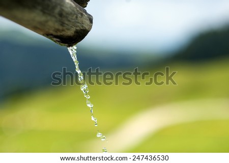 Mountain fresh water of a drinking fountain, with a mountain path in the background.