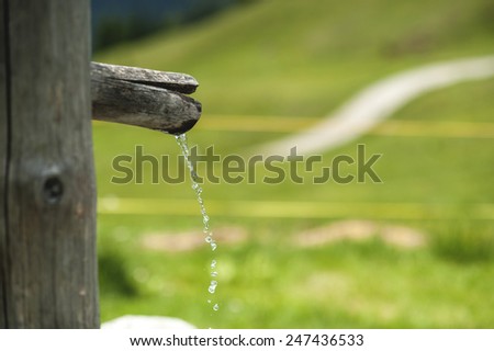 Mountain fresh water of a drinking fountain, with a mountain path in the background.