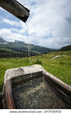 Mountain fresh water of a drinking fountain, with a mountain path in the background, in the Italian Dolomiti mountains.