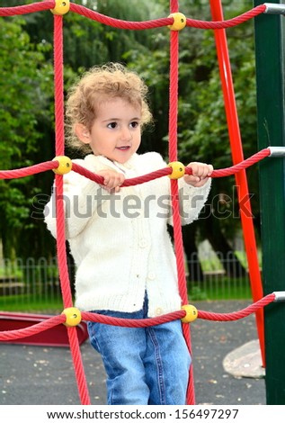 Young child, girl, playing on a rope climbing frame at the playground in the park.