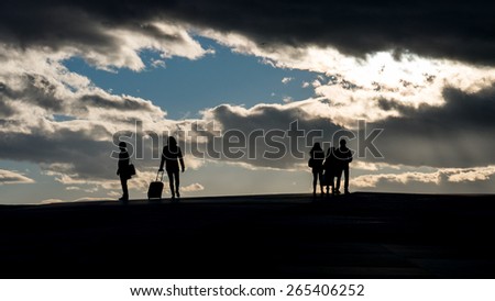 Man standing silhouetted to cloudy skies. Could be a traveler packed and ready with his trolley. Ready to travel with train or plain. Sunny skies in the background